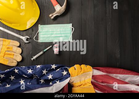 Happy Labor Day beim Ausbruch des Coronavirus. Mehrere Konstrukteurswerkzeuge, Handschuh mit ergreifender US-amerikanischer Flagge, Labor COVID-19-Impfstoff, medizinisch Stockfoto