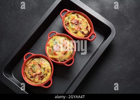 Omelette mit Speck, geriebenem Parmesan und Gemüse in Keramikkokotte auf der Ofenplatte. Leckeres Frühstück Stockfoto