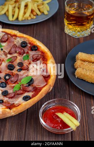 Pizza auf einer Platte Nahaufnahme auf dem Tisch mit Ketchup, Saft, Sauce und Kartoffeln auf einem dunklen Holztisch im rustikalen Stil. Stockfoto