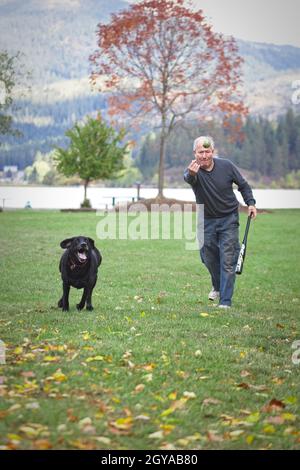 Ein redaktionelles Foto eines Mannes, der mit seinem schwarzen Labrador Retriever in Hauser, Idaho, Fetch spielt. Stockfoto