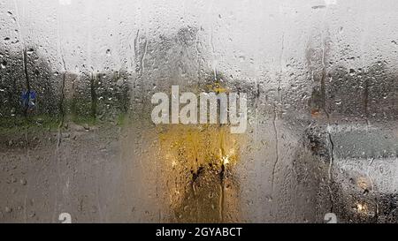 Regen auf die Heckscheibe eines Autos im Herbst. Innenansicht der Straße mit sich bewegenden Autos in der Stadt durch das Fenster aus dem Auto mit Regentropfen. Driv Stockfoto