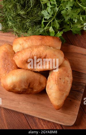 Russische Patties (Pasties, heiße Kuchen, Pirozhki, Pies) auf Holzschrank . Traditionelle hausgemachte gebratene Kuchen mit Kartoffeln Stockfoto