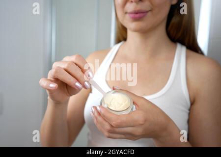 Unkenntlich Mädchen Anwendung Creme aus Glas mit hygienischen Spatel im Badezimmer. Selektiver Fokus. Stockfoto
