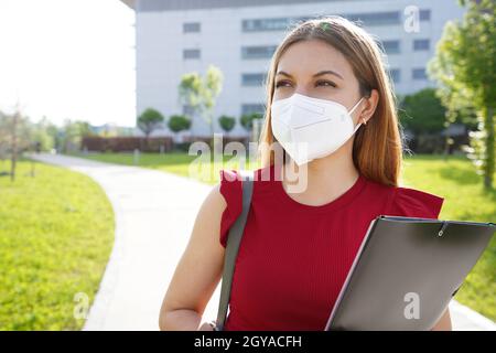 Universitätsstudentin Mädchen mit FFP2 KN95 Gesichtsmaske hält Ordner auf der Seite im Freien suchen Stockfoto