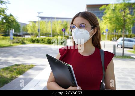 Schöne Student Mädchen trägt FFP2 Schutzmaske zu Fuß in der modernen Straße Stockfoto