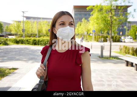 Reflektierende junge Frau in einer leeren Straße in der Stadt, die eine Schutzmaske trägt und zur Seite schaut Stockfoto