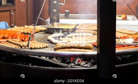 Gebratene Würstchen. Straßenrestaurant. Viele gegrillte Würstchen auf einem großen runden Grill auf einem Street Food Festival. Barbecue-Grill am Food-Stand Weihnachten Stockfoto