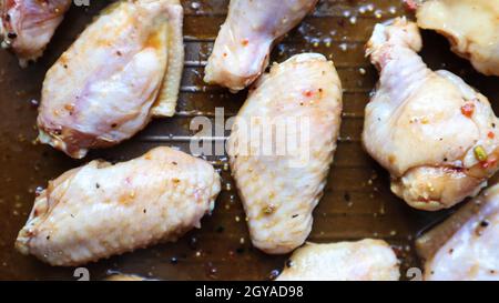 Rohes eingelegtes Huhn Teriyaki Flügel in einer Pfanne vor dem Braten. Ein paar rohe Hähnchenflügel auf einem Backblech. Hühnerfleisch in Öl und Gewürzen in einer schwarzen Pfanne Stockfoto