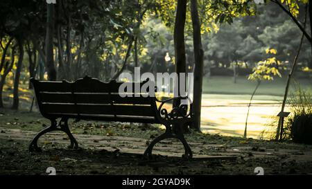 Leere Holz Parkbank mit Blick auf einen See oder Teich. Entspannend ruhigen abgelegenen Bank neben einem Fluss gegen helles grün hinterlegt. Great Outdoor su Stockfoto