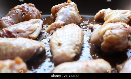 Rohes eingelegtes Huhn Teriyaki Flügel in einer Pfanne vor dem Braten. Ein paar rohe Hähnchenflügel auf einem Backblech. Hühnerfleisch in Öl und Gewürzen in einer schwarzen Pfanne Stockfoto