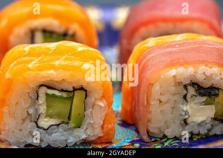 Kalifornische Sushi-Rollen mit Avocado, Gurke und Käse, eingewickelt in Lachs und Thunfisch Stockfoto