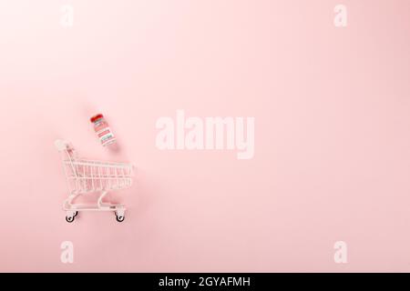 Warenkorb mit Impffläschchen Flaschen und Spritzen zur Impfung gegen Coronavirus, Medizinerkrankung, COVID-19-Impfstoff isoliert auf rosa Stockfoto