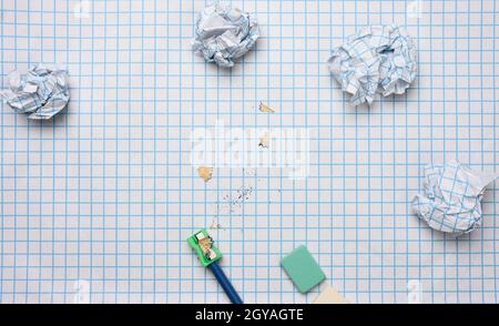 Zerknitterte Papierkugeln und ein geschärfter Holzstift mit Spalten auf einem karierten Papierblatt Stockfoto