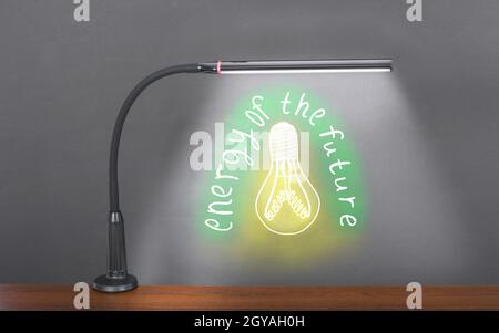 Flexible moderne Tisch-LED-Leuchte leuchtet auf einer gezeichneten grünen Glühlampe mit der Aufschrift „Energie der Zukunft“. Energiesparkonzept. Hohe Auflösung Stockfoto