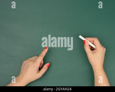 Hand hält ein Stück weiße Kreide auf dem Hintergrund einer leeren grünen Kreidetafel, Präsentationskonzept, zurück zur Schule Stockfoto