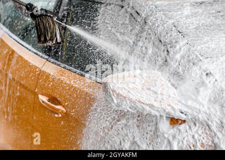 Gelbe auto Spiegel komplett mit dicken Shampoo Schaum bedeckt, mehr Sprühen aus der Bürste, wenn in der Waschhalle gereinigt. Stockfoto