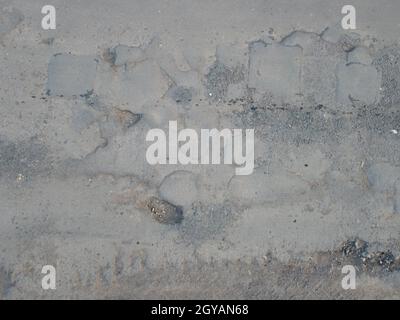 Schlaglöcher auf dem Asphalt. Hintergrund einer kaputten Straße mit Schlaglöchern und Restaurierungspatches. Konzept für Design. Die Textur der beschädigten Straßenoberfläche Stockfoto