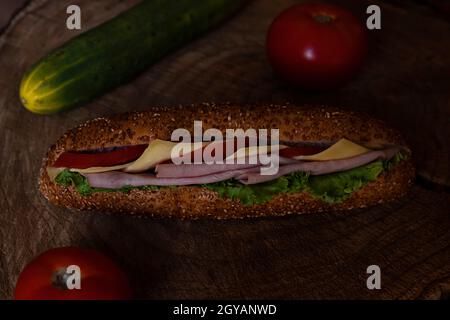 Sandwich mit Salami, Schinken, Salat, Scheiben von frischen Tomaten und Käse auf Holzoberfläche Stockfoto