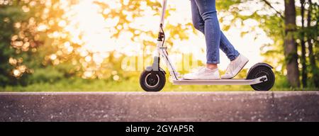 Frau Reiten auf Roller im Park im Sommer. Städtischer Ökotransport Stockfoto