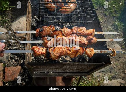 Mann, der Schaschlik oder Schischkebab über Holzkohle vorbereitet. Grillen Sie Fleisch und Würstchen oder Bratwurst auf einem Grillrost im Hinterhof. Gegrilltes Fleisch auf Metallspieß Stockfoto