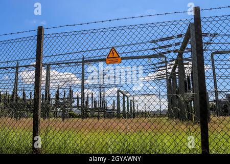 Schild mit den Worten Hochspannung in deutscher Sprache am Zaun eines großen Umspannwerks, das elektrische Energie mit vielen Stromleitungen verteilt Stockfoto