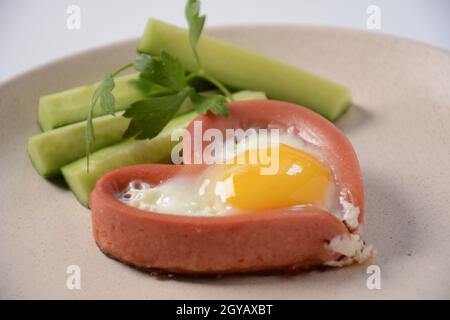 Zwei Würstchen in einem herzförmigen Spiegelei mit grünen Gurken. Frühstück am Valentinstag Stockfoto