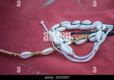 Shell-Knöchelarmband über rotem Segeltuch. Symbol der Sommerzeit Stockfoto