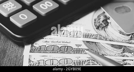 Dollar in 100-Dollar-Scheinen sind auf dem Tisch neben einem Rechner, einer Kreditkarte und einem Stift verteilt. Einhundert-Dollar-Scheine. US-Dollar. Stockfoto