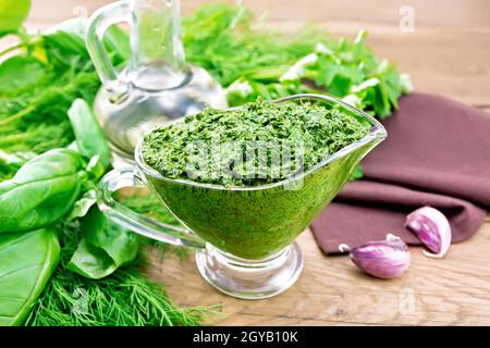 Sauce aus Dill, Petersilie, Basilikum, Koriander, anderen würzigen Kräutern, Knoblauch und Pflanzenöl in einem Glas-Soße-Boot, Serviette auf dem Hintergrund eines alten Holzes Stockfoto