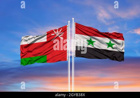 Die Flagge von Oman und Syrien winkt im Wind gegen den weißen, wolkigen, blauen Himmel. Diplomatie Konzept, internationale Beziehungen Stockfoto