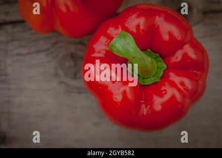 Rote Paprika mit glänzenden Wassertropfen auf rustikalem Holzhintergrund Stockfoto