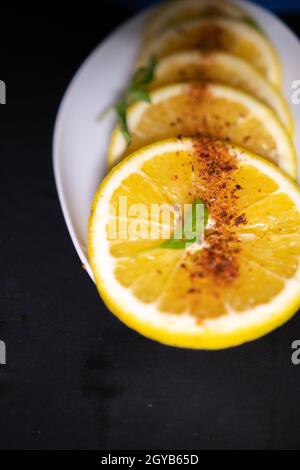 Platte aus orangefarbenen Scheiben mit Chilipulver auf schwarzer Oberfläche Stockfoto