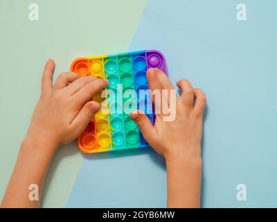 Kinder Hände spielen popit Spielzeug, Draufsicht über zwei Schatten blauen Hintergrund. POPIT auf blauem Hintergrund, Kopierbereich. Beliebte Silikon bunte Anti-Stress Pop it Stockfoto