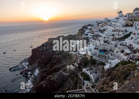 Oia, Santorini, Griechenland - 28. Juni 2021: Weiß getünchte Häuser und Windmühlen in Oia in warmen Sonnenstrahlen auf Santorini. Griechenland Stockfoto