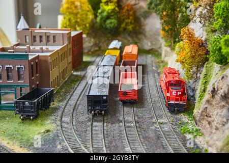 Einige Miniatur-Spielzeugzüge, die Waren auf Bahngleisen neben dem alten westlichen Dorf befördern Stockfoto