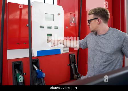 Junger kaukasischer Fahrer mit Sonnenglas, drückt die Nummer auf der Tankmaschine von Tankstellen, um Pickup-Truck aufzutanken. Stockfoto