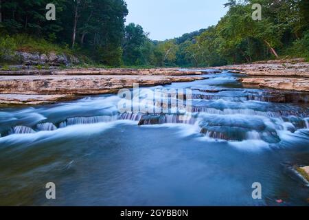 Sommerbäume in einem Wald mit einem verwinkelten Fluss mit wunderschönen Steinen und lebhaften, umgestürzten Blättern Stockfoto