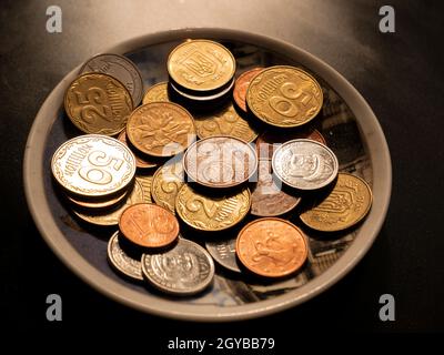 Kleine Geldmünzen in einem Teller auf schwarzem Hintergrund. Eurocent. Ukrainische Griwna. Chinesischer Yuan. Währungseinheit. Kleine Münze. Reichtum. Schatz. Hintergrund Stockfoto