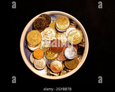 Kleine Geldmünzen in einem Teller auf schwarzem Hintergrund. Eurocent. Ukrainische Griwna. Chinesischer Yuan. Währungseinheit. Kleine Münze. Reichtum. Schatz. Hintergrund Stockfoto