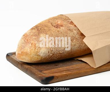 Vollgebackenes ovales Brot aus weißem Weizenmehl in einem Papierbeutel auf einem Holzbrett Stockfoto