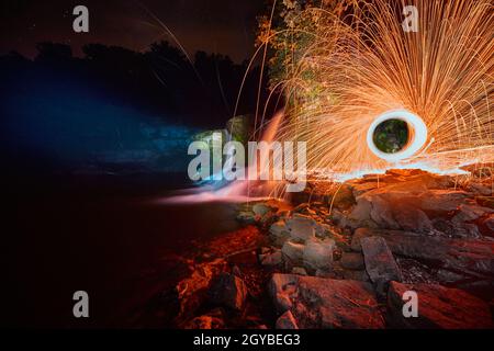 Unheimlich glühender Wasserfall in der Nacht mit einem gelben Funkenorb Stockfoto