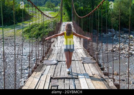 Ein Mädchen in einem gelben T-Shirt läuft auf einer Hängebrücke Stockfoto