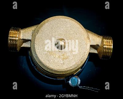 Wasserzähler mit Gewindeanschluss für Muttern. Schwarzer Hintergrund. Sanitäranlagen. Reparatur der Rohrleitungen. Sanitär-Reparaturman. Pipeline. Hintergrundbild. Stockfoto