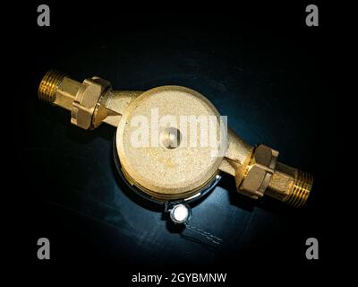 Wasserzähler mit Gewindeanschluss für Muttern. Schwarzer Hintergrund. Sanitäranlagen. Reparatur der Rohrleitungen. Sanitär-Reparaturman. Pipeline. Hintergrundbild. Stockfoto