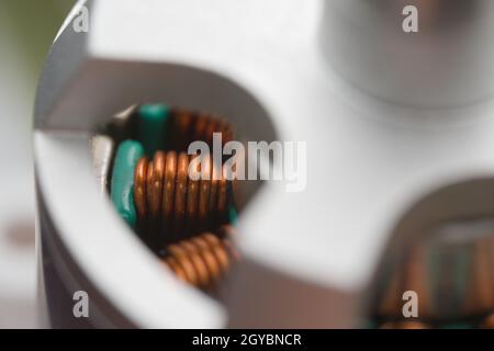 Helle Nahaufnahme von elektromagnetischen Kupferspulen in einem bürstenlosen Drohnenmotor. Staub im Inneren und Metallstrukturen außen. Vollformatbild Stockfoto