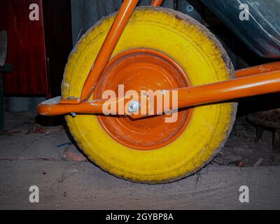 Ein gelber Reifen auf einem Karrenrad. Orangefarbene Scheibe auf einem gelben Rad. Schubkarre für den Garten. Versand. Art des Transports. Reifenservice. Hintergrundbild. Stockfoto