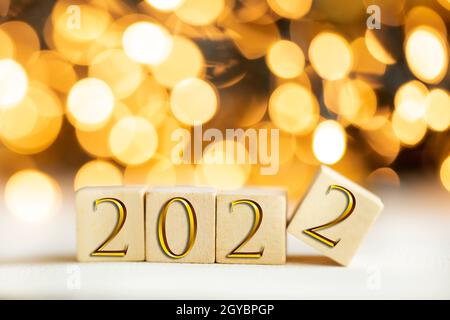 Das Jahr 2022 geschrieben auf Holzwürfeln in goldenen Luxusbuchstaben mit glänzendem Bokeh Hintergrund, Neujahrsfeier Konzept Glitter Stockfoto