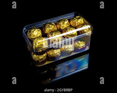 Eine Schachtel runder Pralinen in goldener Verpackung auf schwarzem Hintergrund. Runde Bonbons. Goldene Farbe. Ein Weihnachtsgeschenk. Geburtstag. Food-Foto. Süßes Essen. Ha Stockfoto