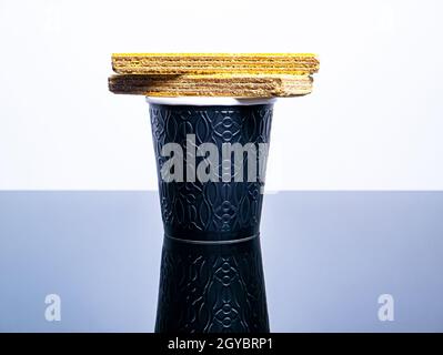 Schwarzer Einwegbecher aus Papier für Kaffeegetränke und Waffelplätzchen auf dem Tisch. Kaffee Getränk Waffel Dessert. Street Cafe. Papierbecher. Einwegtischwar Stockfoto