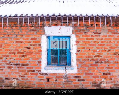 Eiszapfen von gefrorenem Wasser auf dem Dach des Hauses über dem Fenster. Schnee schmilzt. Winter. Frühlingstropfen. Eiszapfen. Gefrorenes Wasser. Ziegelwand. Frostiger Fr Stockfoto